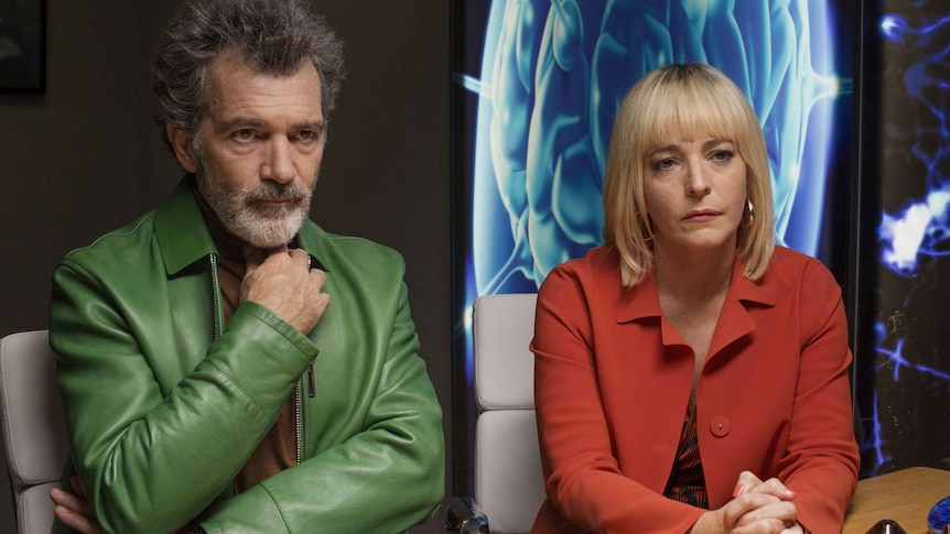 Colour still of Antonio Banderas and Nora Navas sitting side by side at a conference table in 2019 film Pain and Glory.