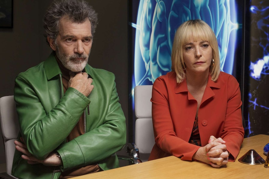 Colour still of Antonio Banderas and Nora Navas sitting side by side at a conference table in 2019 film Pain and Glory.