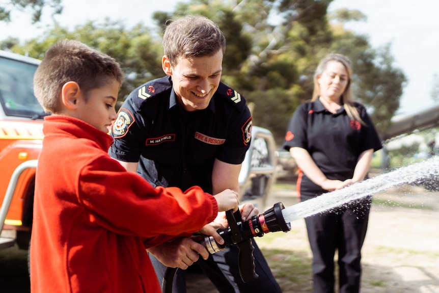 A close-up shot of firefighter Michael Hatfield holding a fire hose with a student from Mosman Park School for Deaf Children.