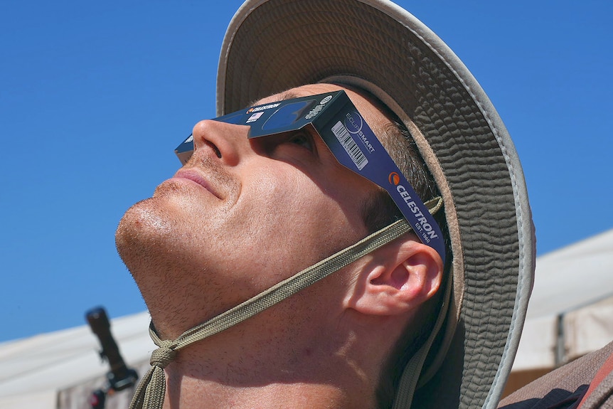 A man is looking up at the solar eclipse wearing solar eclipse glasses