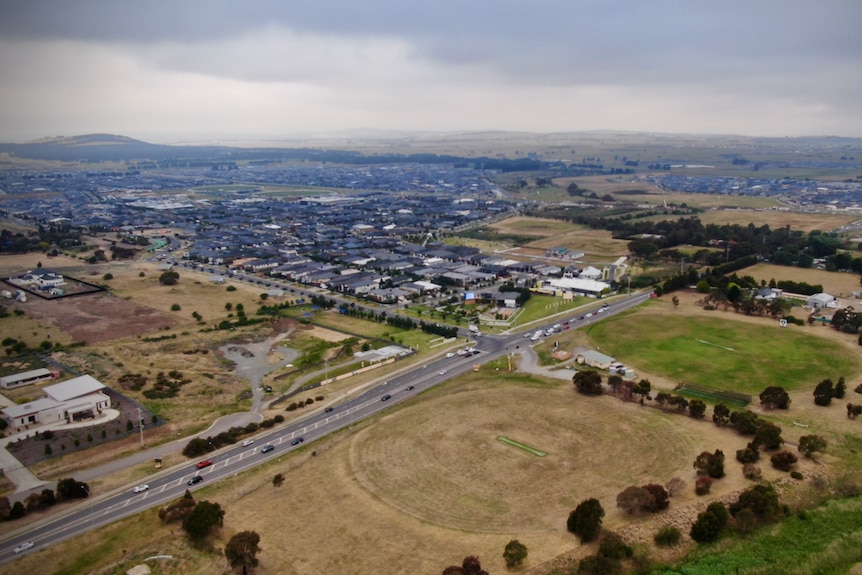 A wide shot taken from a drone showing a road dividing a new estate and grassland on a cloudy day.