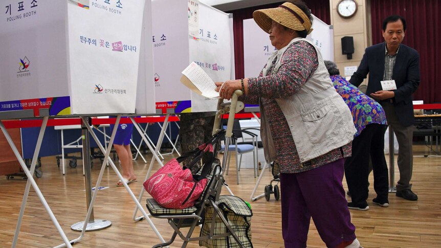 An older woman, with a walker, makes her way towards a polling both with her ballot paper in-hand.