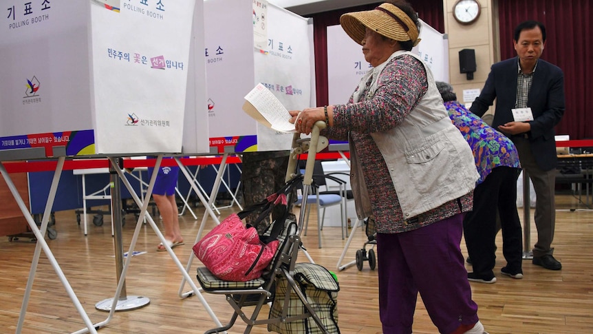 An older woman, with a walker, makes her way towards a polling both with her ballot paper in-hand.