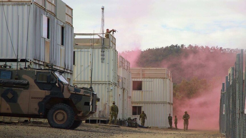 A camouflage army tank is parked in front of a building with pink smoke in the background and four sold