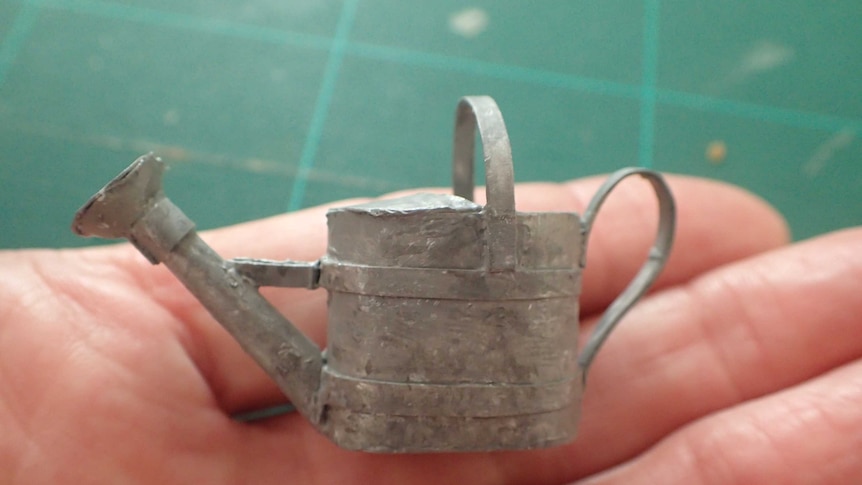 A hand holds a miniature metal watering can.