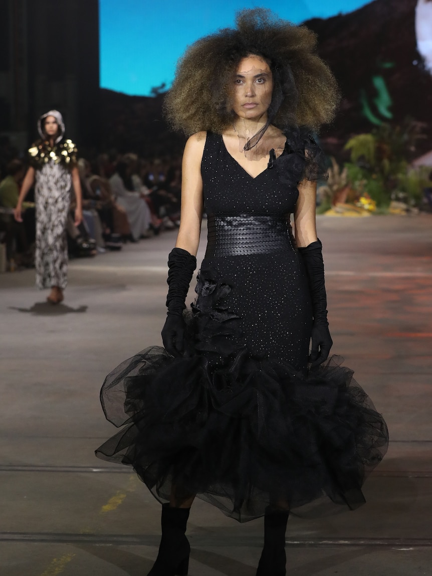 Indigenous model wears extravagant all-black dress on the fashion runway.
