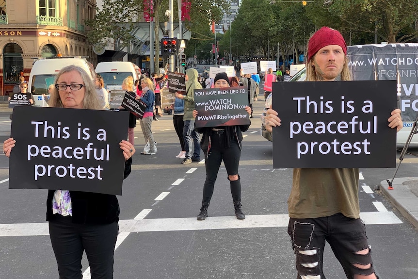 Protesters holding signs reading 'this is a peaceful protest' block Flinders Street.