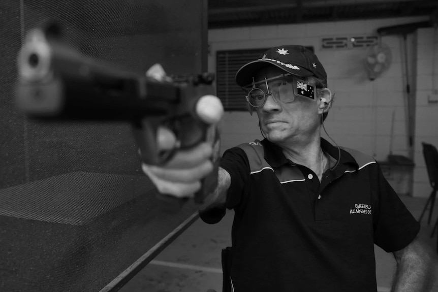 A black and white photograph of a man aiming a pistol