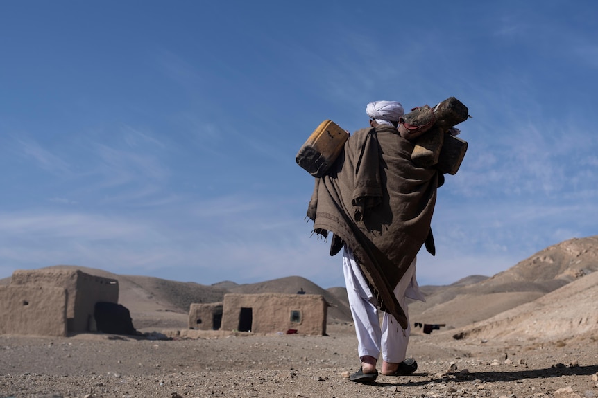 Hajj Wali lleva paquetes sobre sus hombros mientras camina hacia sus casas en una aldea en las afueras de Herat, Afganistán.