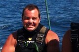 Ruben McDornan sits on the edge of a boat after diving, smiling and looking tan.