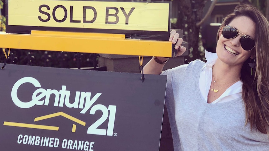 Laura Polin standing in front of her home next to a 'sold' sign.