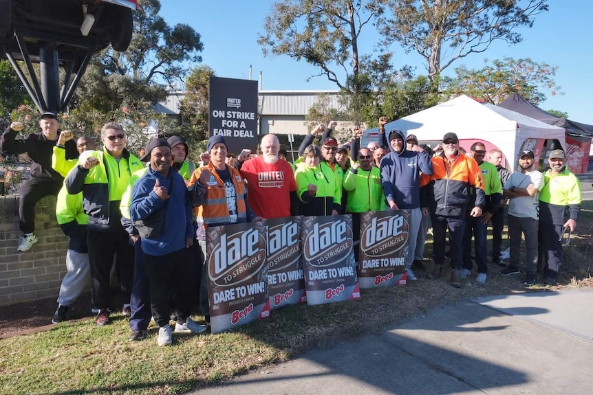 A group of dairy workers in high vis holding Dare iced coffee signs, striking for more pay outside.