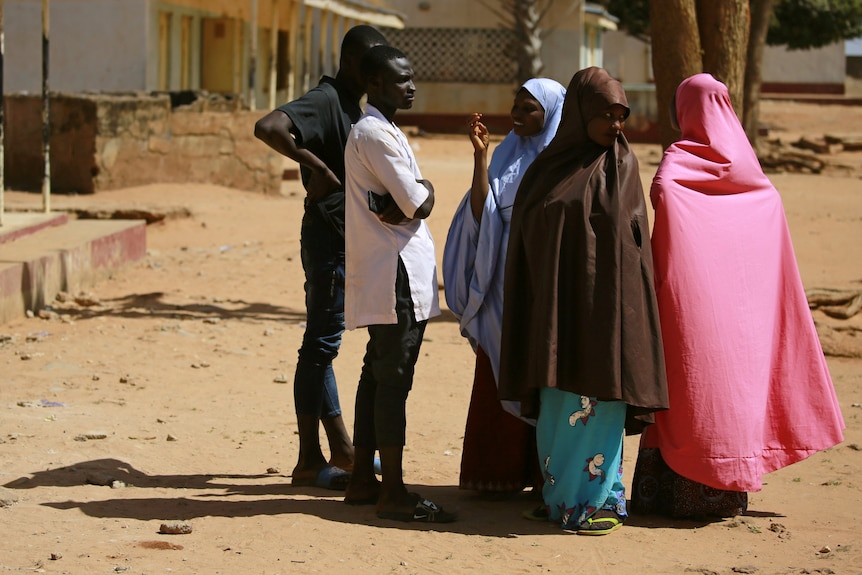 Three women and two women stand outside a school.