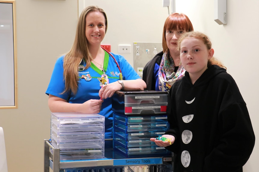 Toni Grayson holds comforting, sensory objects in the hospital, while standing with her mother and a doctor.