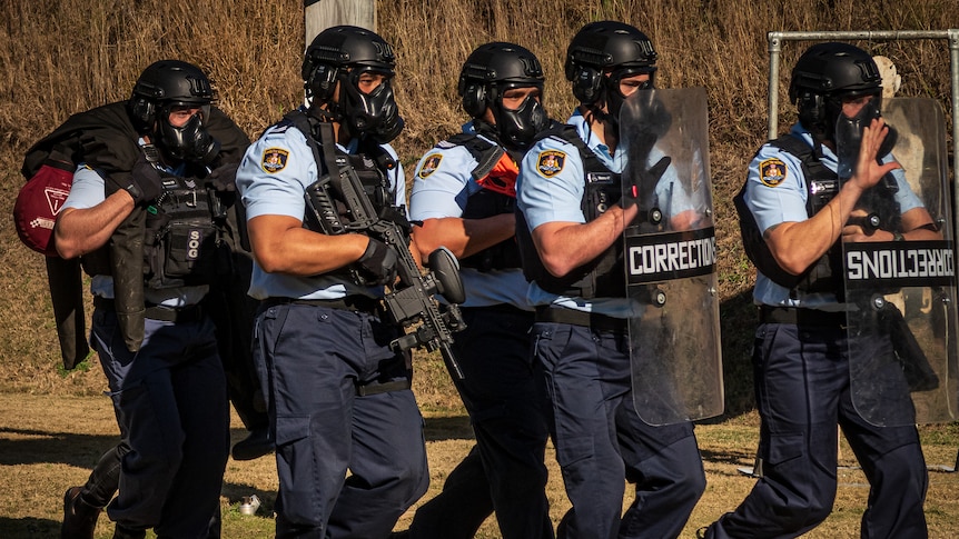 A group of men in protective gear and weapons carrying a training dummy.
