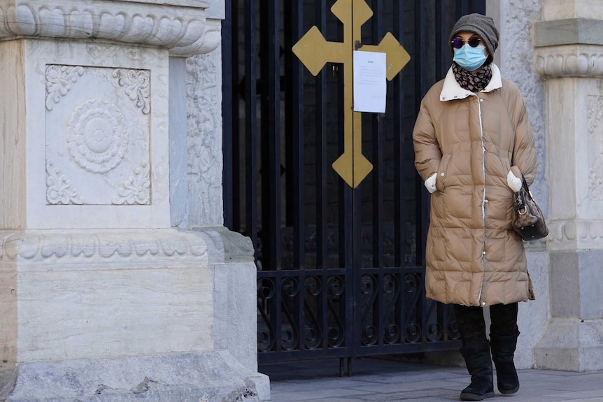 A woman in a mask wasks in front of church door.