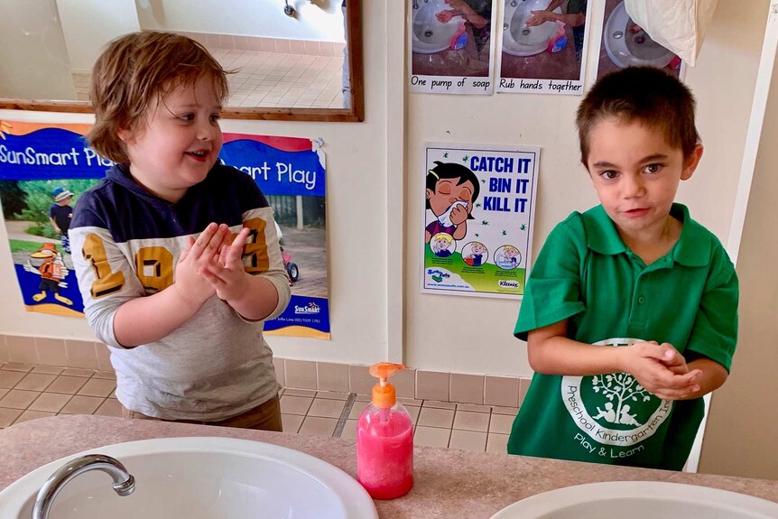 Two young boys washing hands at sink in bathroom smiling.