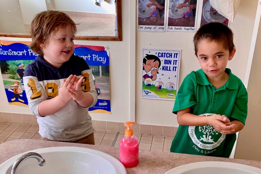 Two young boys washing hands at sink in bathroom smiling.