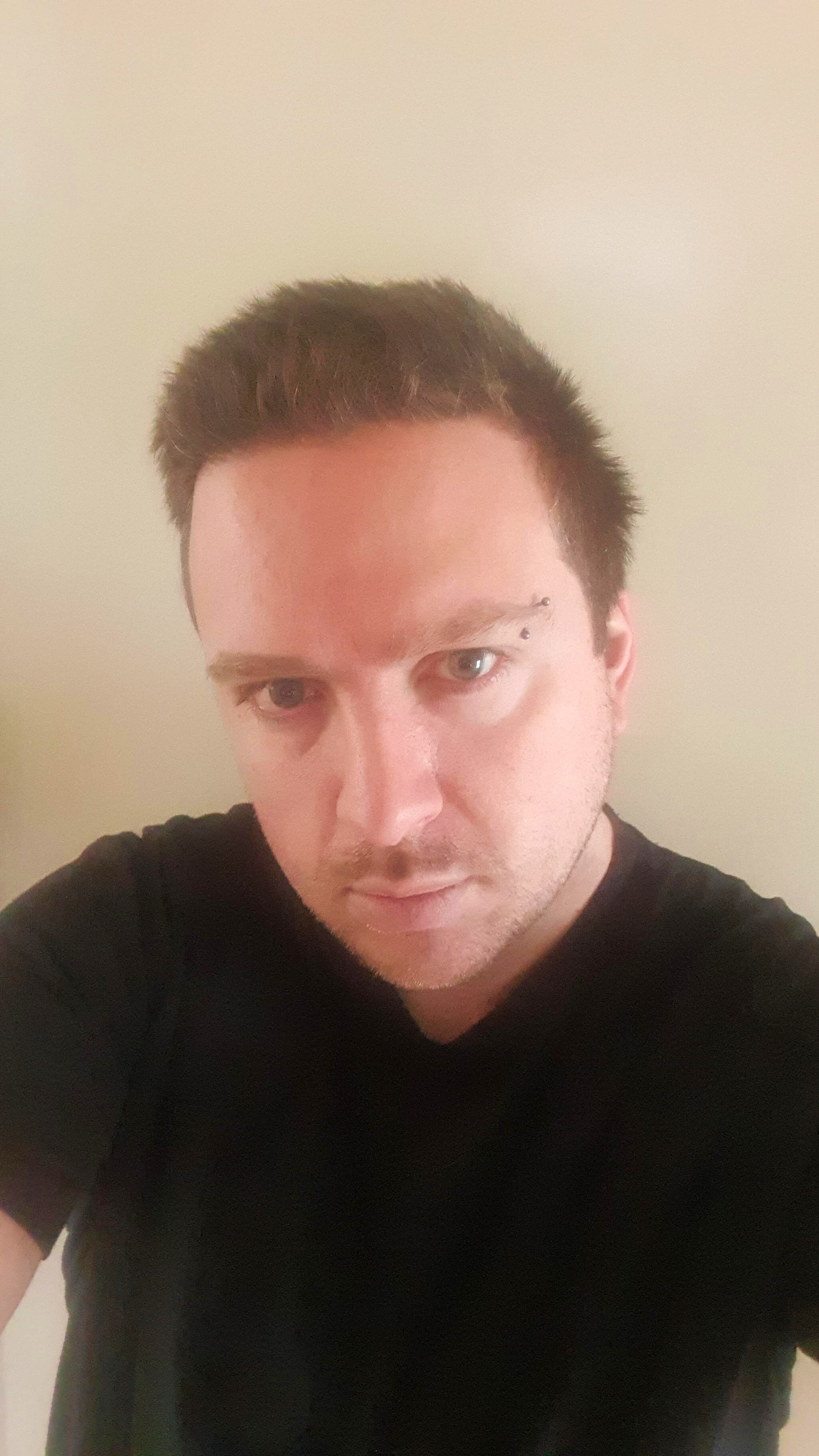 A selfie of a man in his 30s with eyebrow piercing and black tshirt