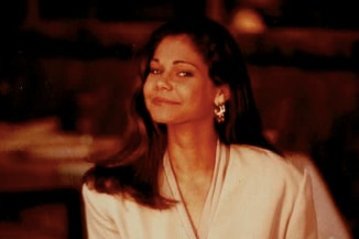 A young woman with long brown hair at a dining table smiling