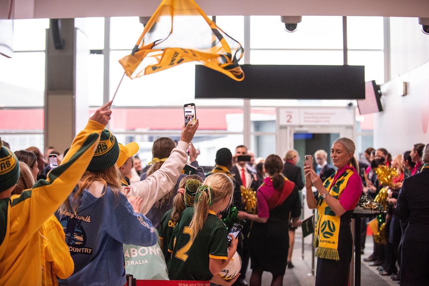 a group of matilda soccer fans wait at the airport for the team as they wave flags and banners
