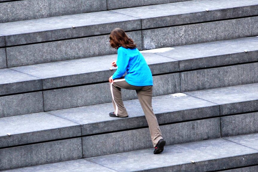 A young girl in a blue top and track pants climbs large concrete steps.