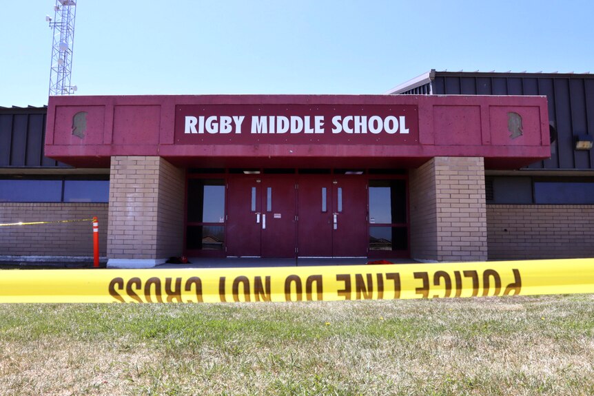 A line of police tape in the foreground in front of a building with the words Rigby Middle School above the door