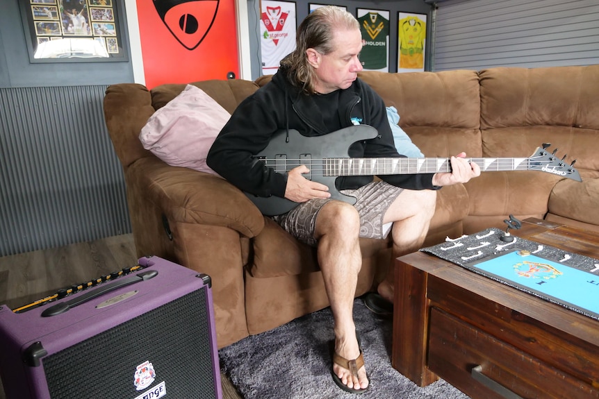 Man sits on a brown lounge and plays an electric guitar 