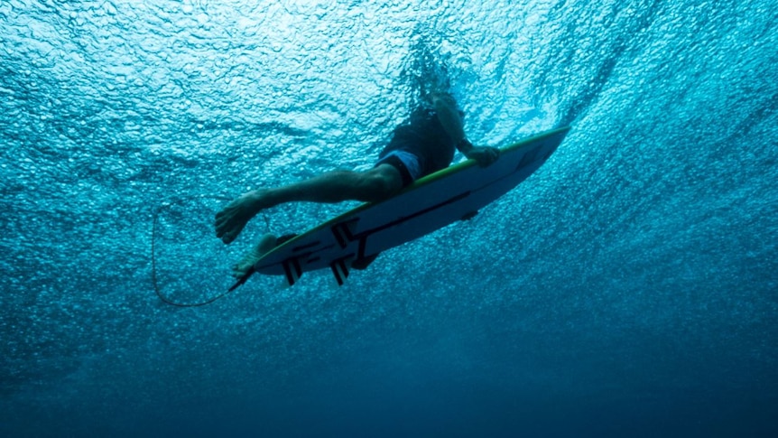 under water shot of man on surfboard with shark personal protection device