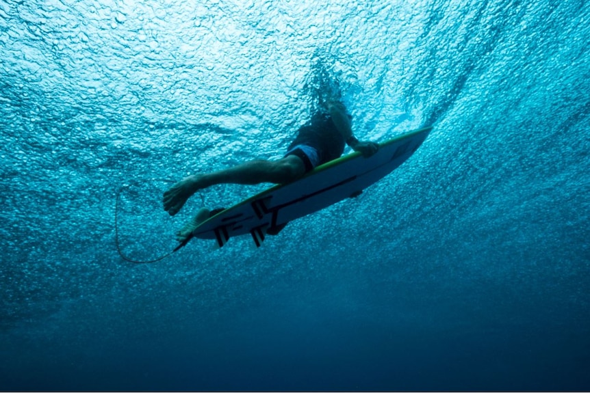 An under water shot of man on surfboard with shark personal protection device.