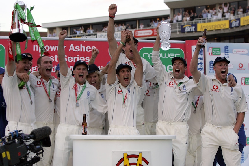 Michael Vaughan lifts up the Ashes urn, he's surrounded by his teammates who have their arms raised, celebrating. 