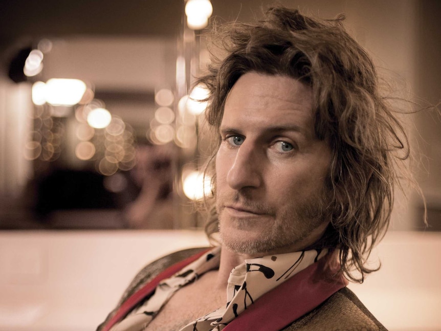 You Am I member, radio presenter and memoirist Tim Rogers leaning back and staring into the camera, lights in the background