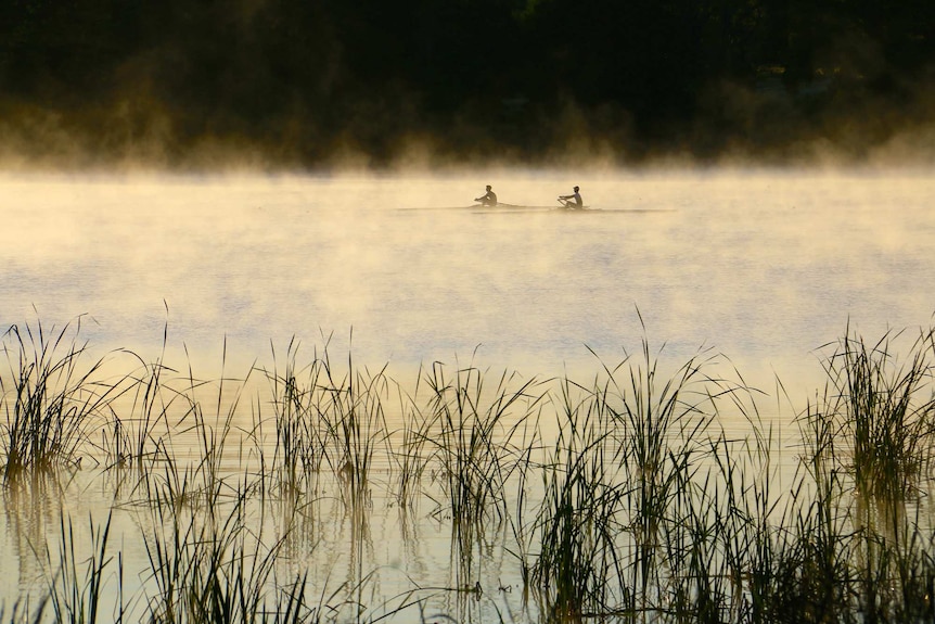 Two people row on a river as mist rises.