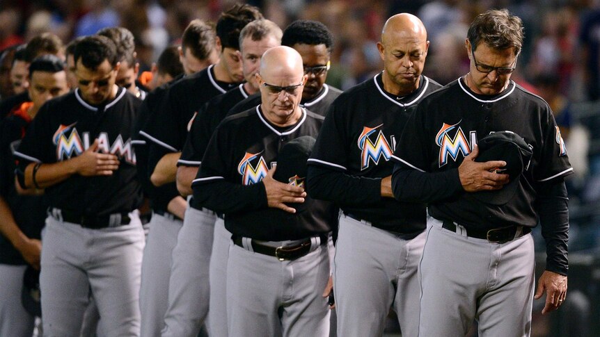 Members of the Miami Marlins stand with their caps over their hearts before a game.