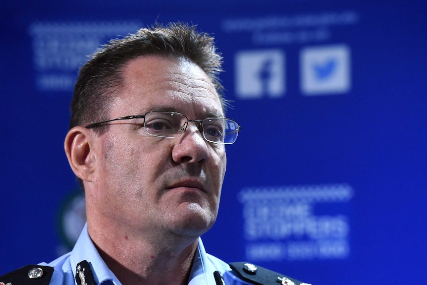 The head of a dark-haired police officer wearing rimless glasses and standing in front of a Crime Stoppers poster