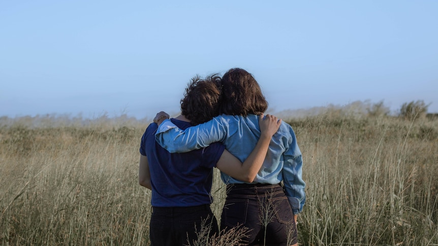 Two women, with their backs to the camera have their arms around each other showing support.