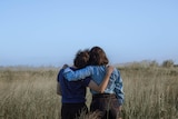 Two women, with their backs to the camera have their arms around each other showing support.