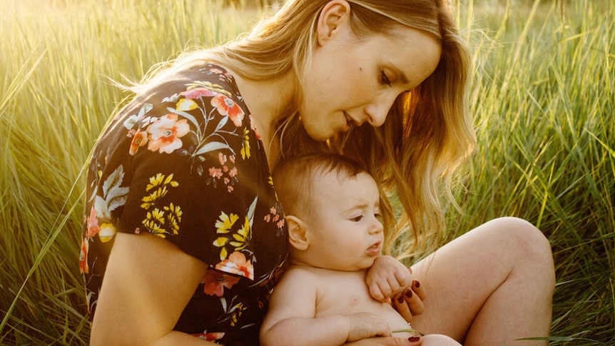 A mother and her baby sitting in a grassy field.