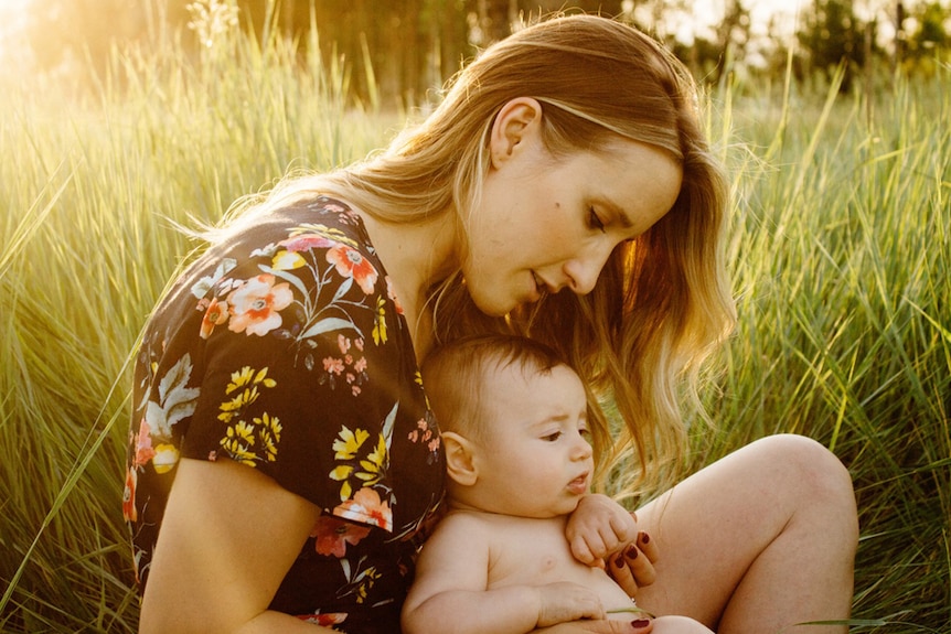 A mother and her baby sitting in a grassy field.