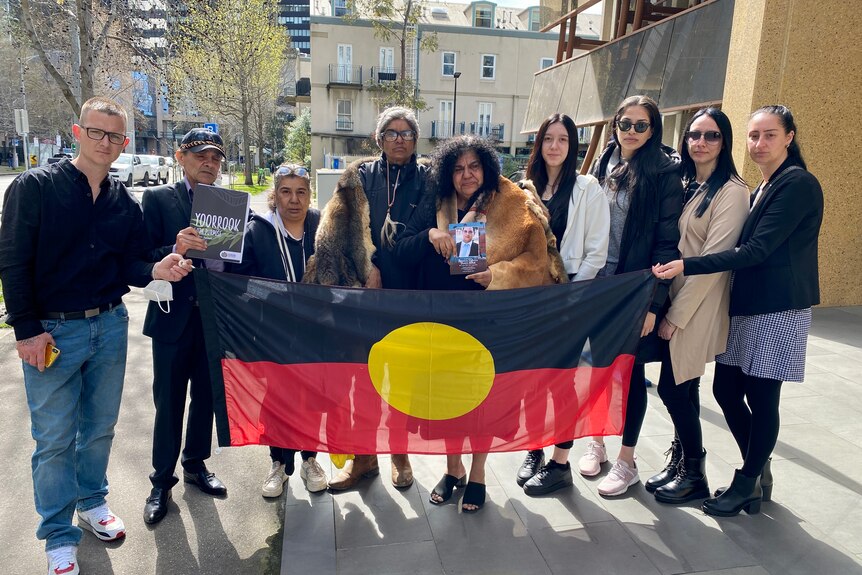 A group of people hold an Aboriginal flag and a photo of a young man.