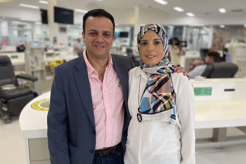 A man in a suit and a woman wearing a head scarf smiling at the camera. 