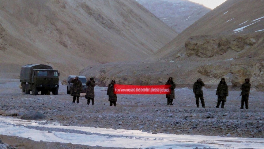 Chinese troops hold a banner which reads "You've crossed the border, please go back".