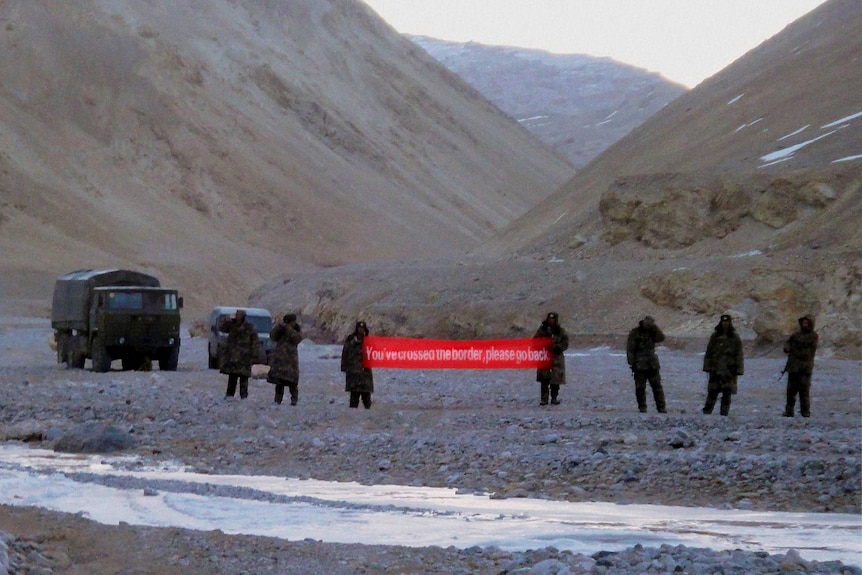 Chinese troops hold a banner which reads "You've crossed the border, please go back".