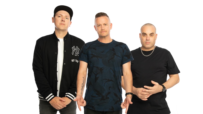 Three men stand against a white background looking towards the camera