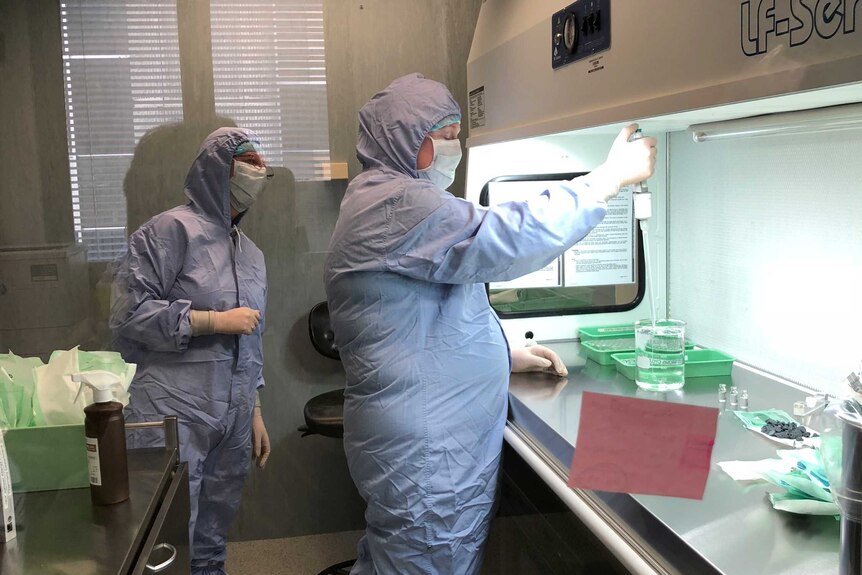 Picture of two people in full blue protective suits wearing face masks in a lab.