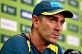 Justin Langer, in his Australian training gear, purses his lips as he answers a question at a press conference.