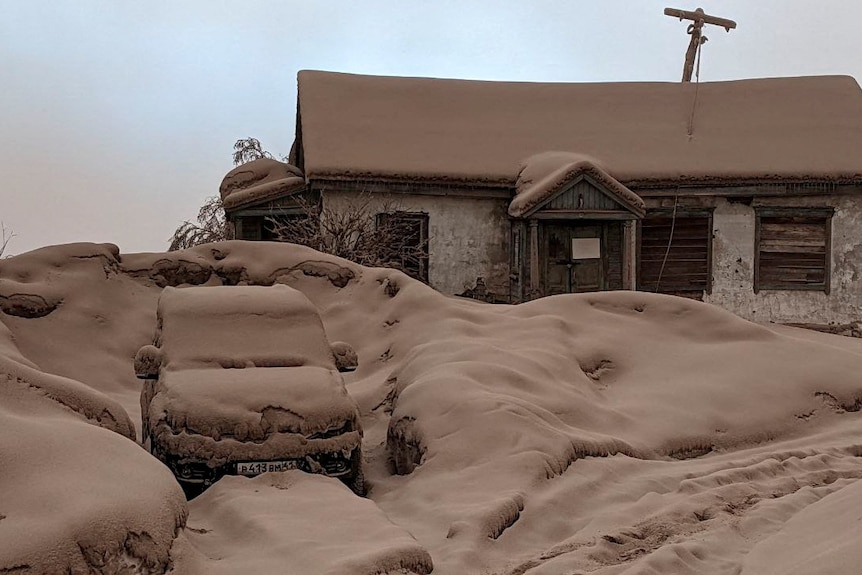 A house and car are buried under a thick covering of brown volcanic dust.
