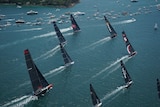 Yachts sail near land, with smaller boats in the background, as part of the 2019 Sydney to Hobart yacht race