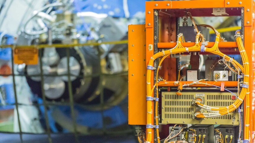 A bright orange box with wires sprouting out of it. In the background, part of the gyroscope that keeps the telescope stable.