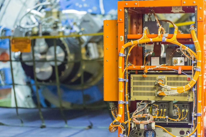 A bright orange box with wires sprouting out of it. In the background, part of the gyroscope that keeps the telescope stable.